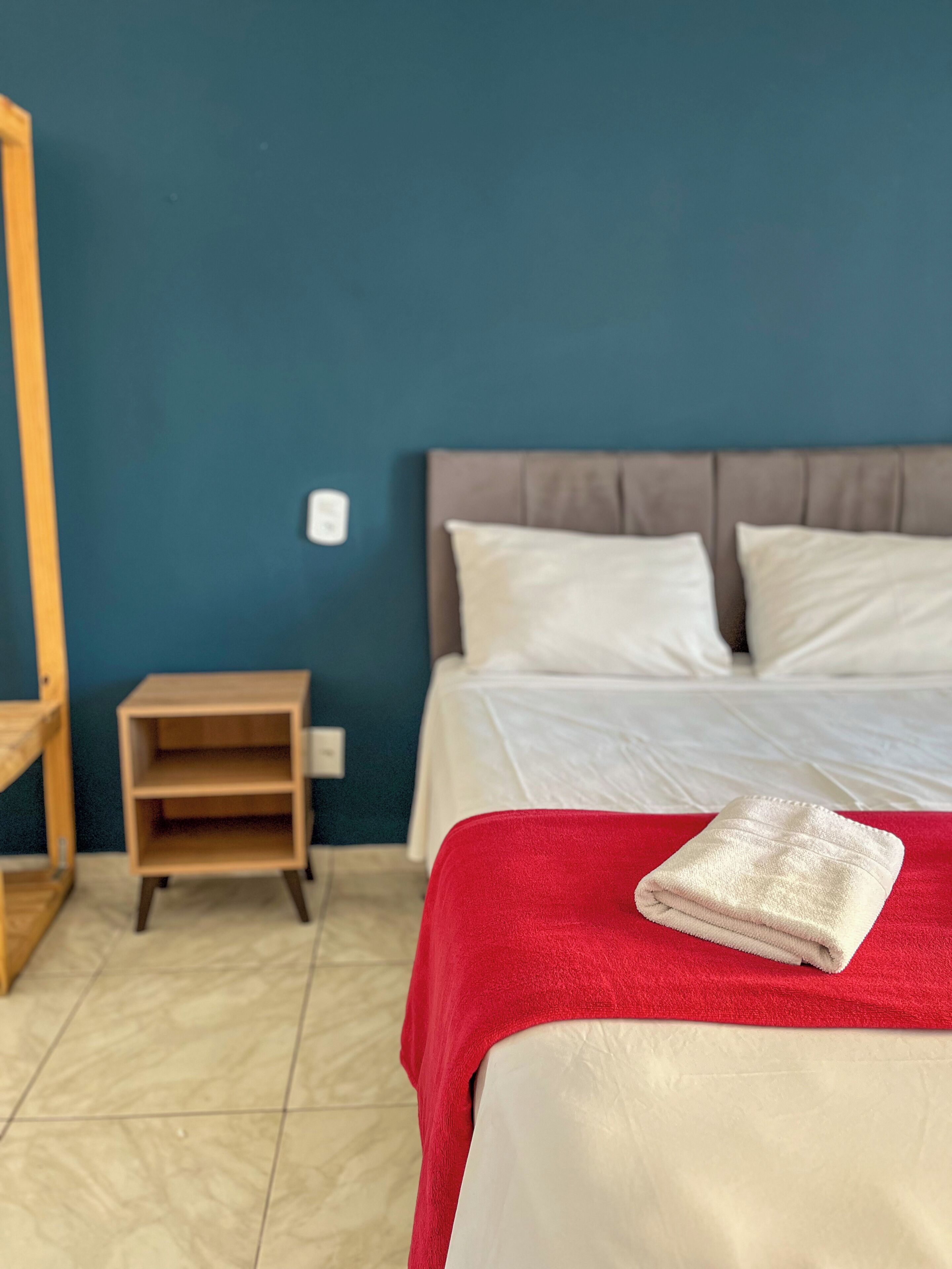 A hotel room with a bed, a nightstand, and a red blanket.