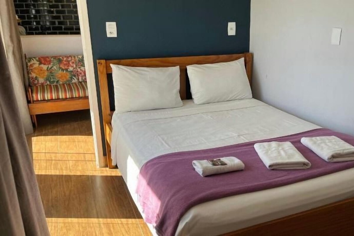 A single bed with a wooden frame, white bedding, and a purple throw blanket.
