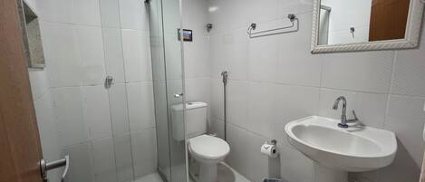 Un baño con ducha de vidrio, inodoro, lavamanos y espejo.