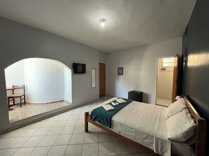A bedroom with a bed, a TV, a small cabinet, and a door leading to another room. - Pousada Vila Appia (Cabo Frio)