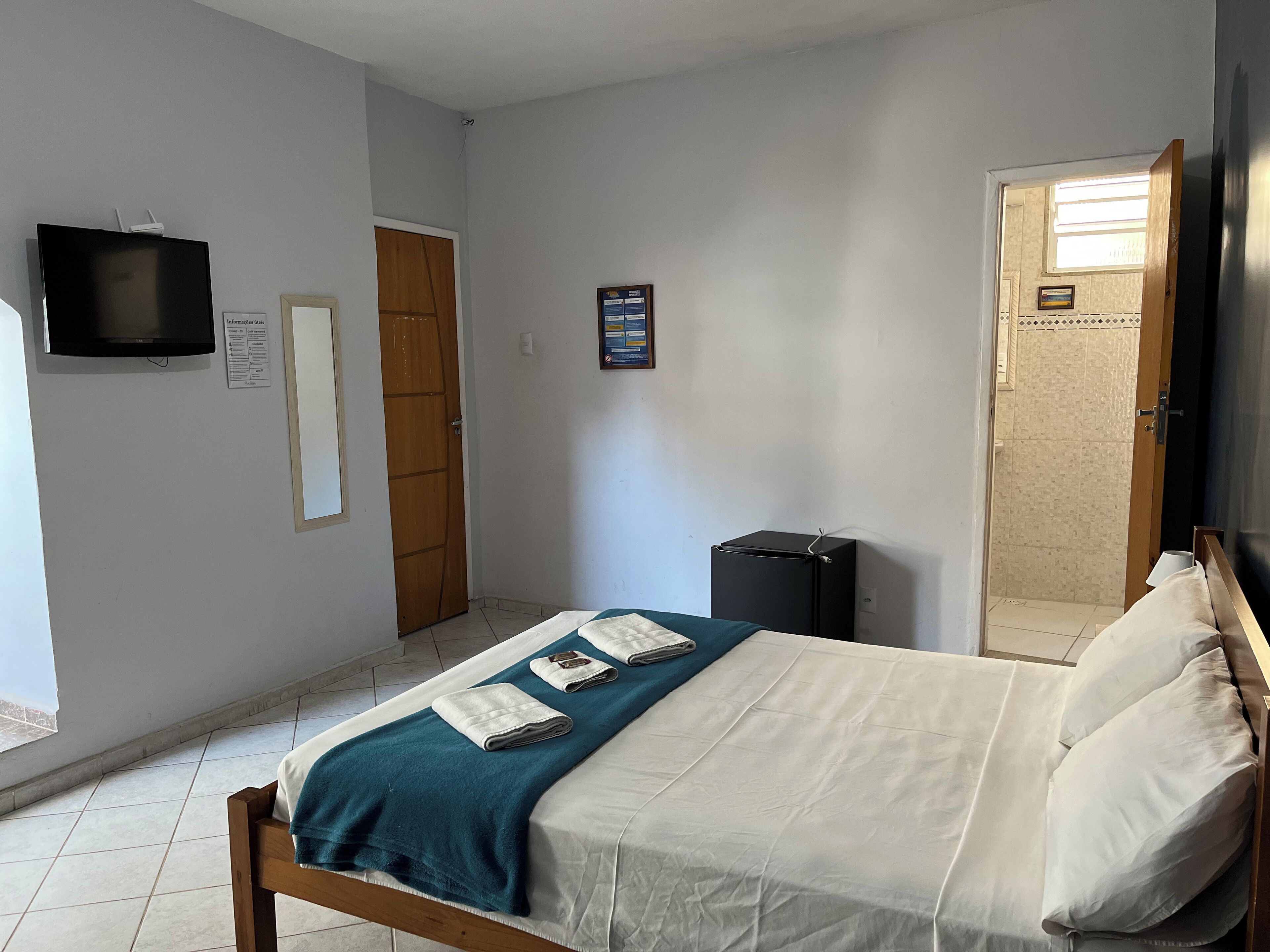 A hotel room with a bed, a TV, a door, and a small cabinet.