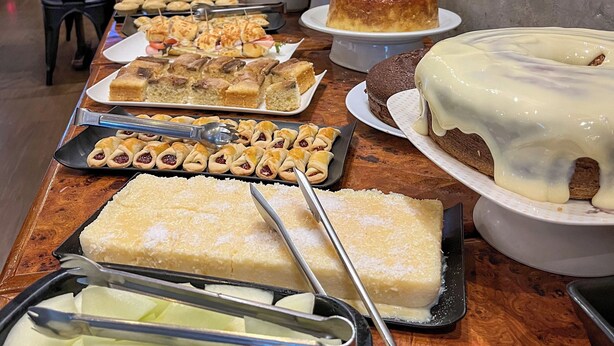 Een buffet met diverse desserts en een televisiescherm waarop een zonsondergang te zien is.