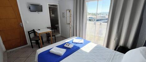 Une chambre d’hôtel équipée d’un lit, d’un bureau, d’une chaise, d’une télévision et d’une fenêtre avec des rideaux.