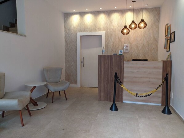 A reception area with a wooden desk, two chairs, a small table, and a herringbone-patterned wall. - Pousada Vila Appia (Cabo Frio)