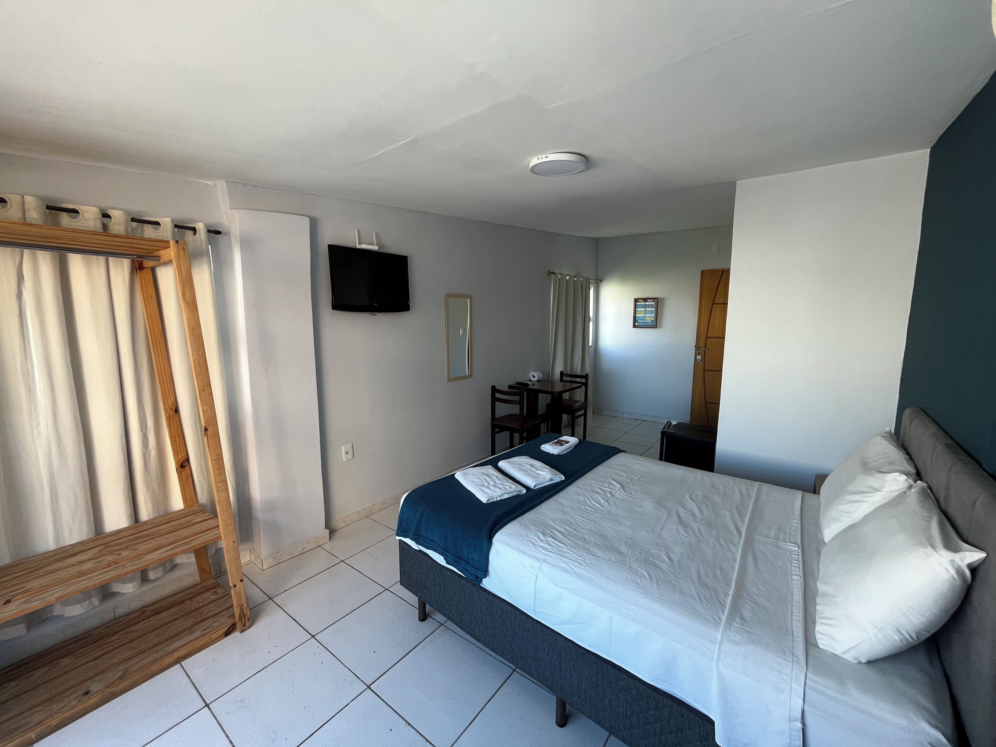 Une chambre d’hôtel avec un lit, un bureau, une chaise, une télévision et une fenêtre avec des rideaux.