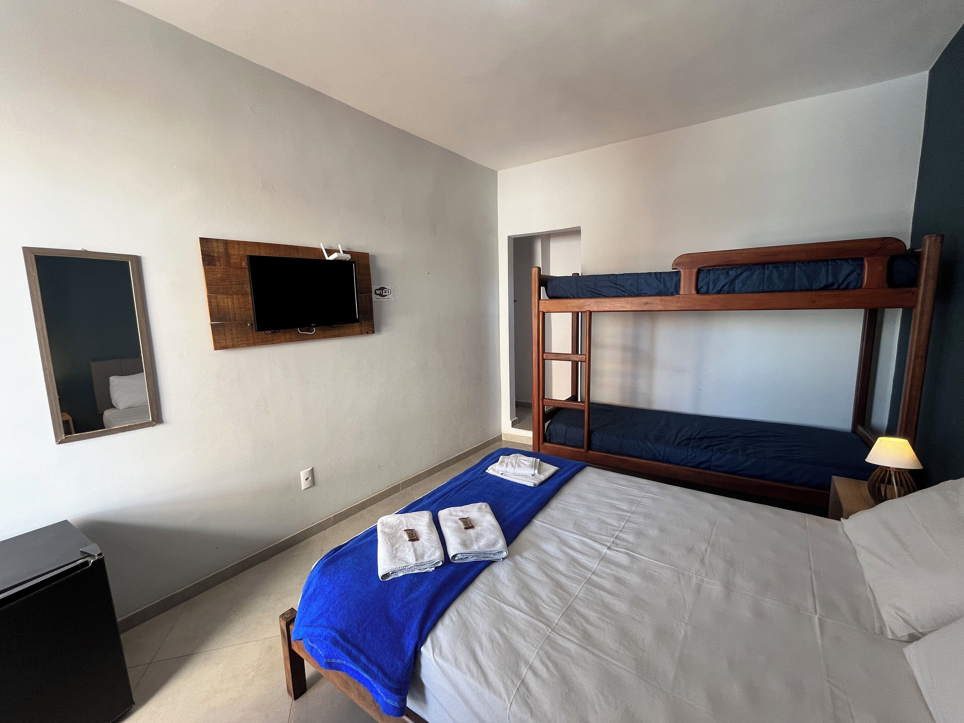 A bedroom with a bunk bed, a flat-screen TV mounted on the wall, a desk with a chair, and a lamp on the side table.