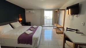Een hotelkamer met een bed, een bureau, een televisie en een schuifdeur naar een balkon.