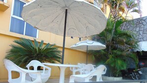 Outdoor seating with white plastic chairs and tables, a large umbrella, and a stone wall with a motorcycle parked nearby. - Alvorada Palace Hotel (Cuiabá)