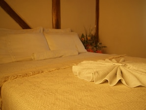 A neatly made bed with a folded towel, a white pillow, and a decorative plant in the background. - Pousada Martin Pescador (Bombinhas)