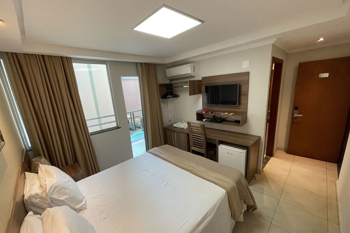 A hotel room with a bed, desk, chair, TV, and a small refrigerator.