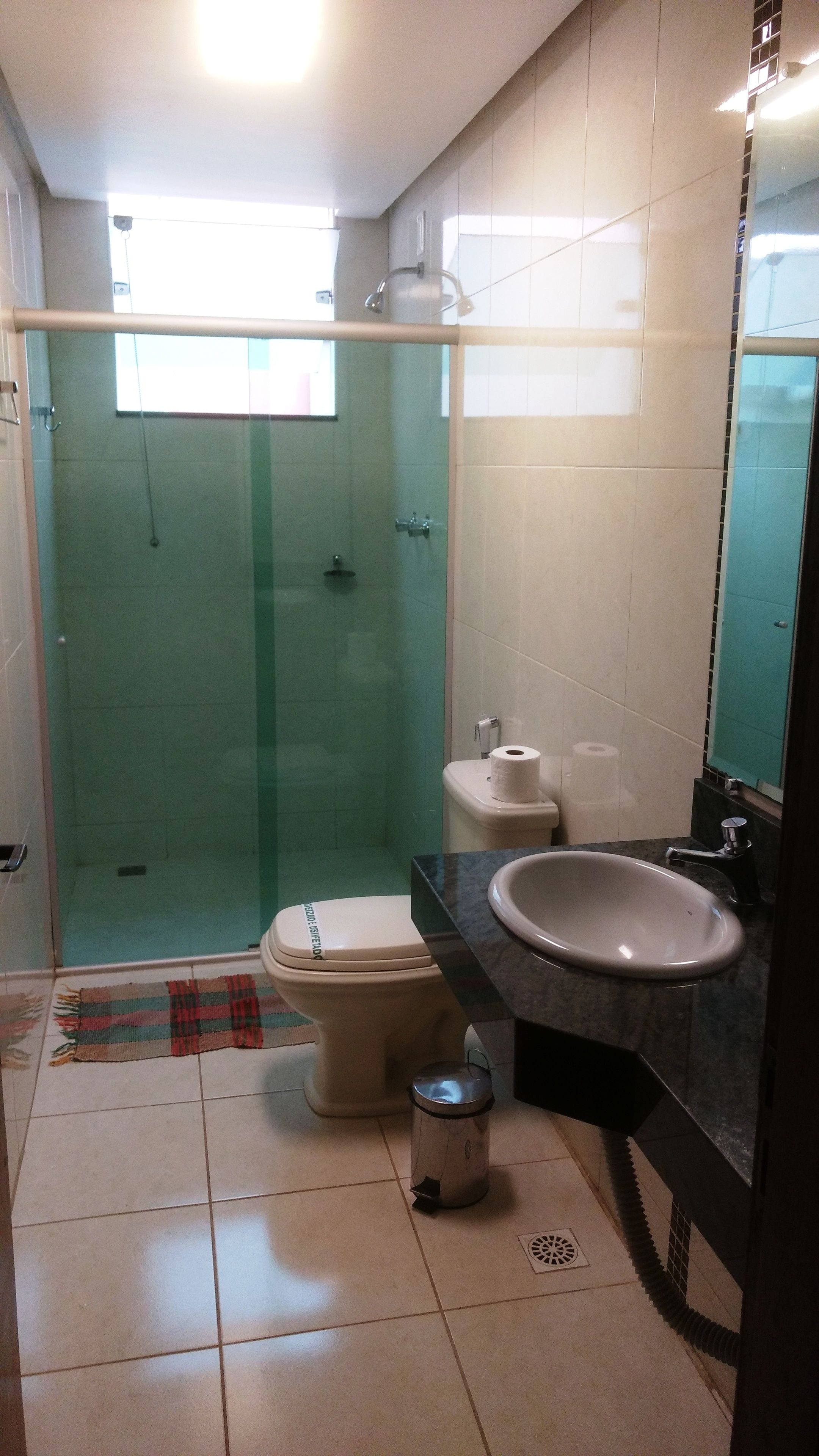 Un baño con ducha envuelta en vidrio, inodoro, lavamanos y espejo.