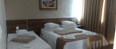 A hotel room with two single beds, a wooden headboard, a nightstand with a lamp, and a painting on the wall.