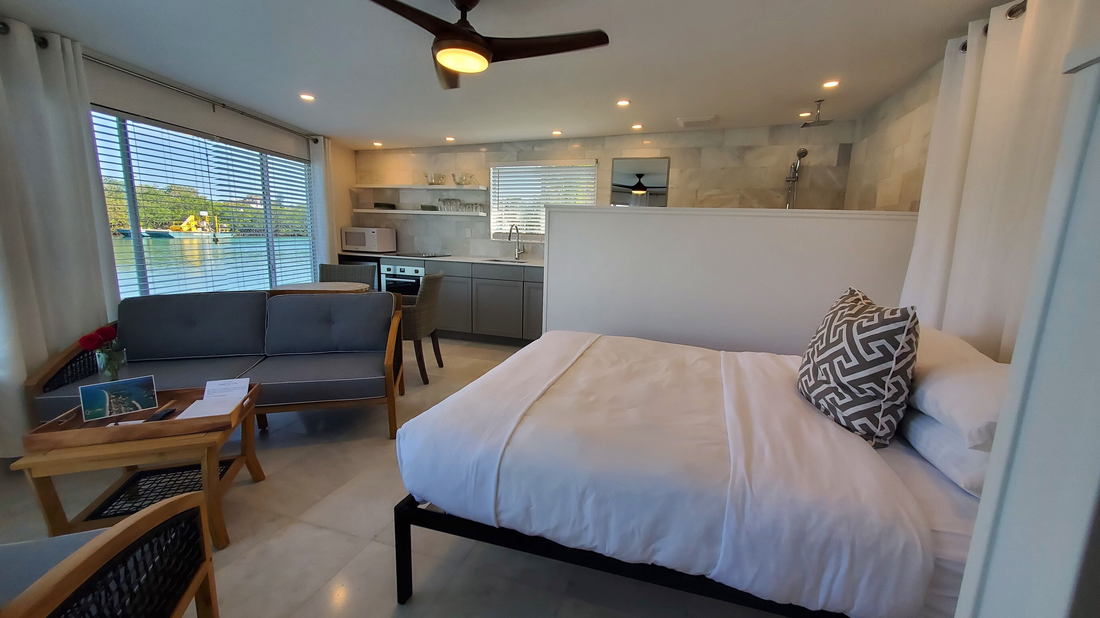 Een moderne hotelkamer met een bed, een bank, een klein tafeltje met dienblad en een kitchenette op de achtergrond.