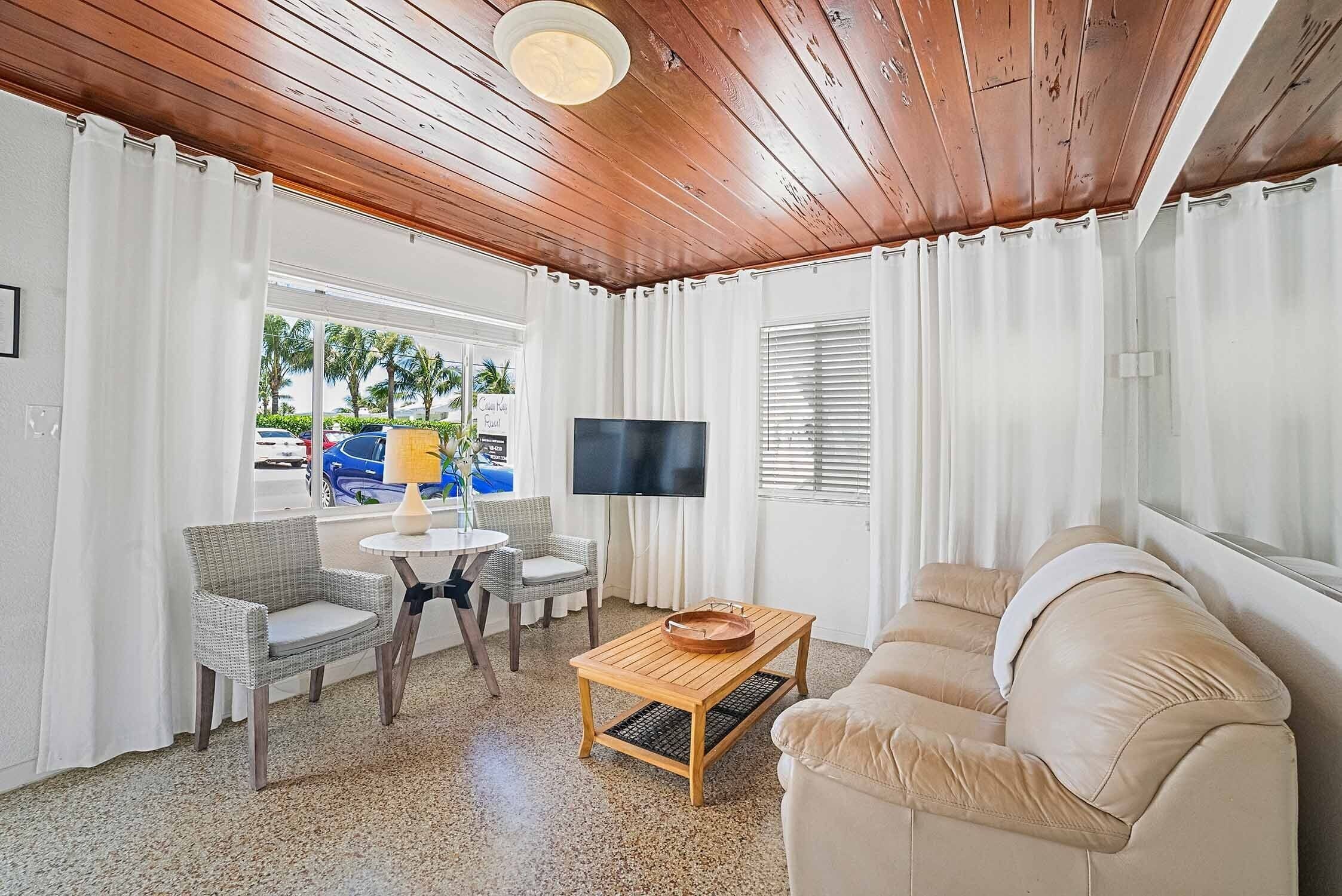Sala de estar com teto de madeira, sofá bege, televisão e área de jantar com mesa e cadeiras.