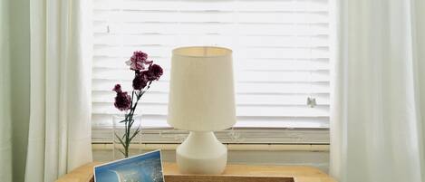 A wooden tray with a lamp, a postcard, and a menu on a table by a window with white curtains.