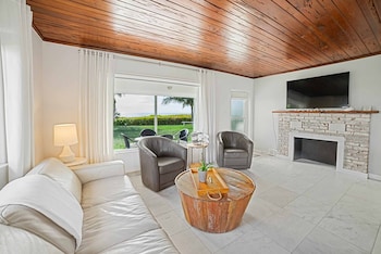 A bedroom with a wooden ceiling, a TV mounted on the wall, a bed with white bedding, and a view of a garden through an open door. at Casey Key Resort 