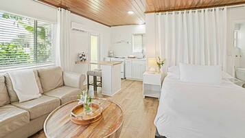 A modern hotel room with a wooden ceiling, a sofa, a bed, a dining area, and a kitchen.