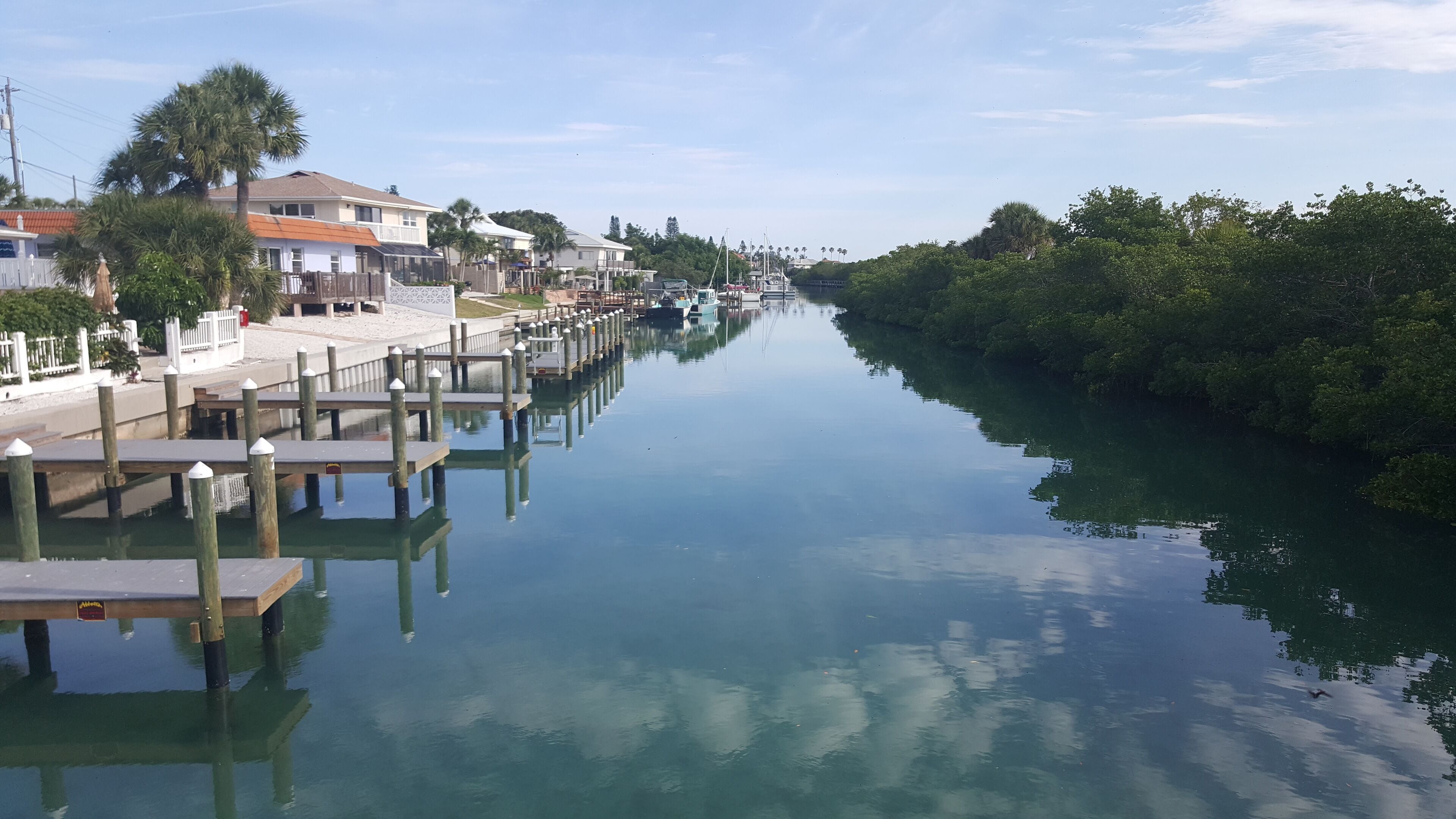 A calm waterway with docks, houses, and dense greenery along the banks.