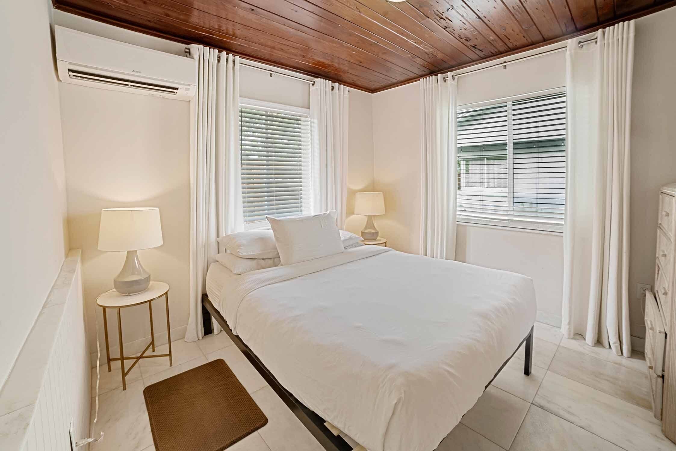 A bedroom with a bed, two bedside tables with lamps, a radiator, and a window with blinds.