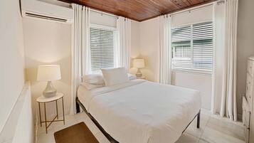 A bedroom with a bed, two bedside tables with lamps, a radiator, and a window with blinds.