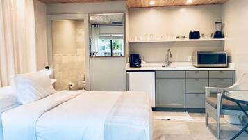 A bedroom with a bed, a chair, a kitchenette with a microwave, and a ceiling fan.