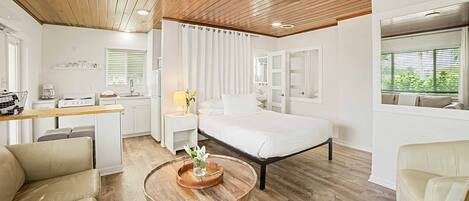 Un dormitorio moderno con techo de madera, una cama grande, una mesita de noche con lámpara y vistas al exterior a través de una ventana.