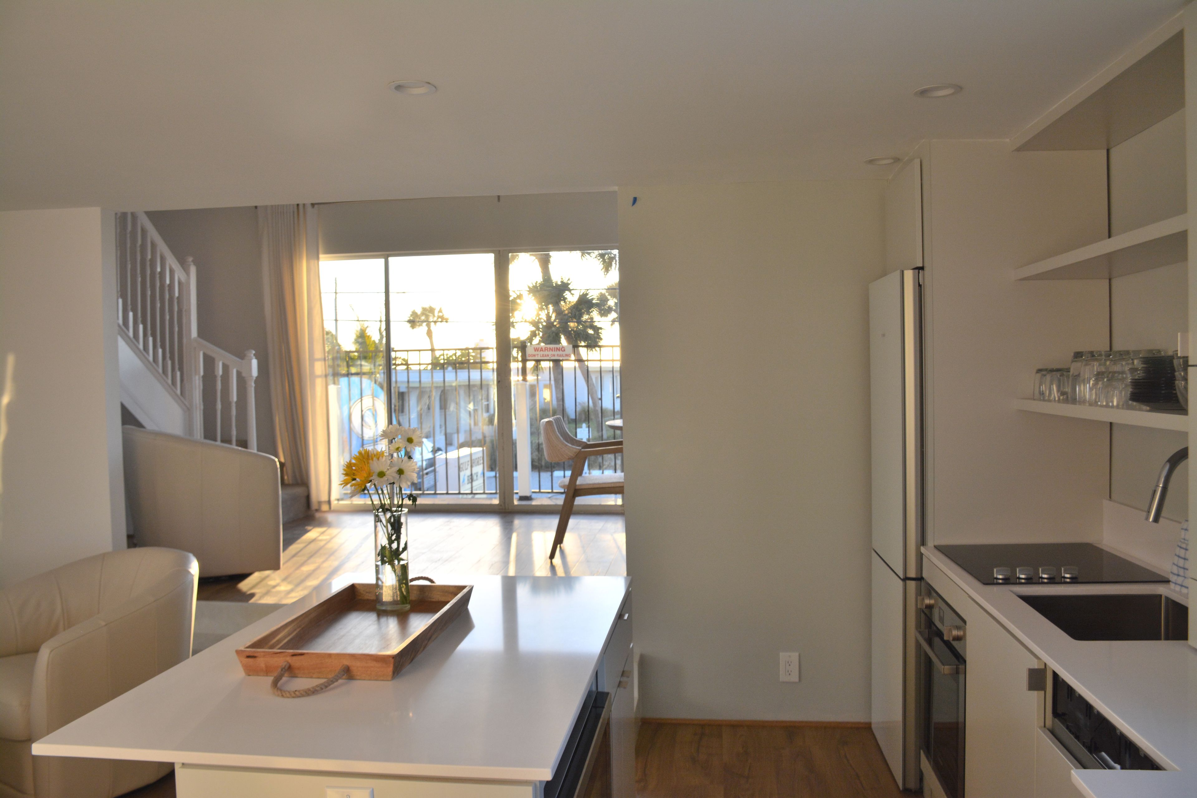 Una cocina moderna con una isla central, un comedor con sofá y vistas al exterior a través de amplios ventanales.