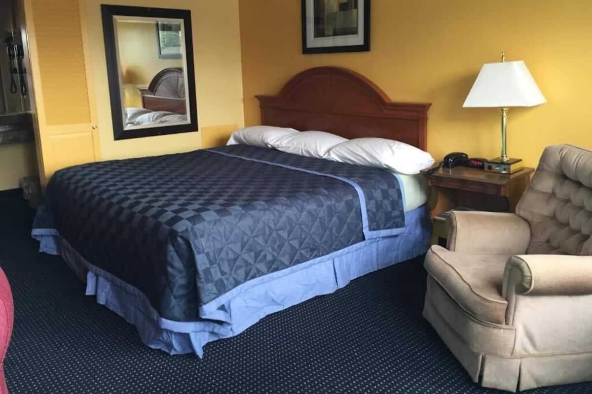 A hotel room with a bed, a chair, a nightstand, and a lamp.