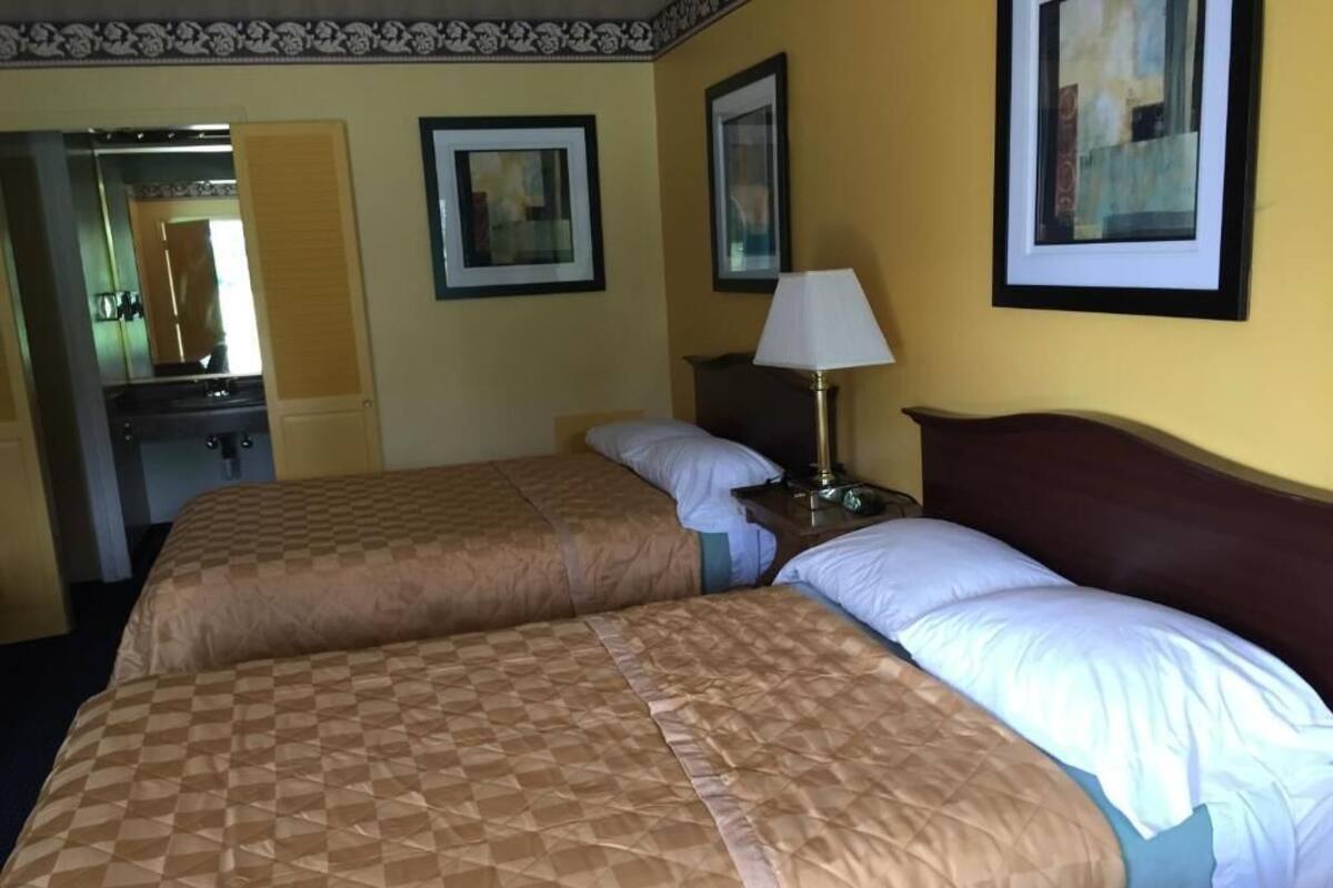 A hotel room with two beds, a nightstand, a lamp, and framed artwork on the walls.
