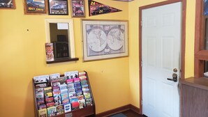 A room with a yellow wall, a framed map, a framed picture of a race car, and a display of travel guides. - Norwalk Inn (Norwalk)