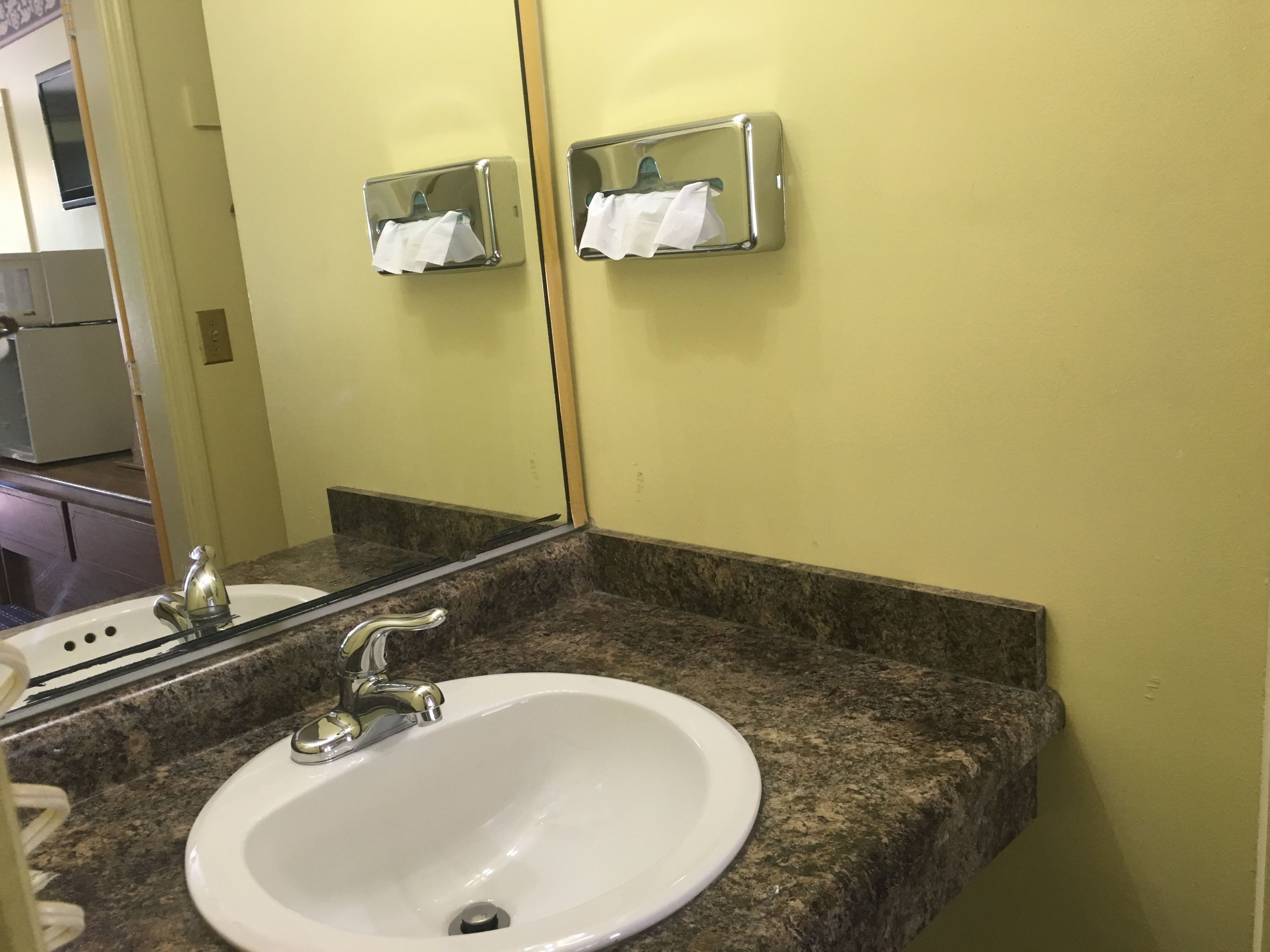 A bathroom with a white sink, granite countertop, and a mirror reflecting a towel dispenser.