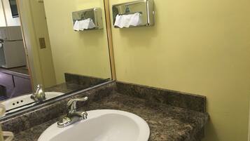 A bathroom with a white sink, granite countertop, and a mirror reflecting a towel dispenser.