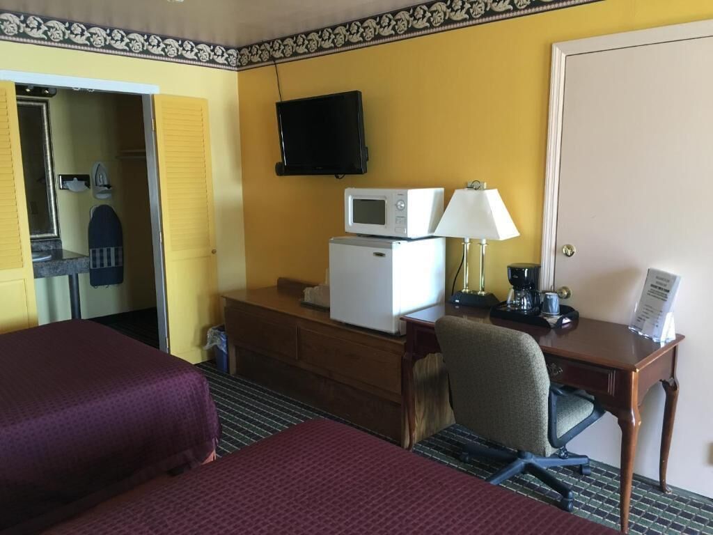 A hotel room with two beds, a desk with a computer, a microwave, and a TV on the wall.