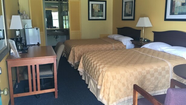 A hotel room with two beds, a desk, a chair, a mirror, and a small table with a lamp. - Norwalk Inn (Norwalk)