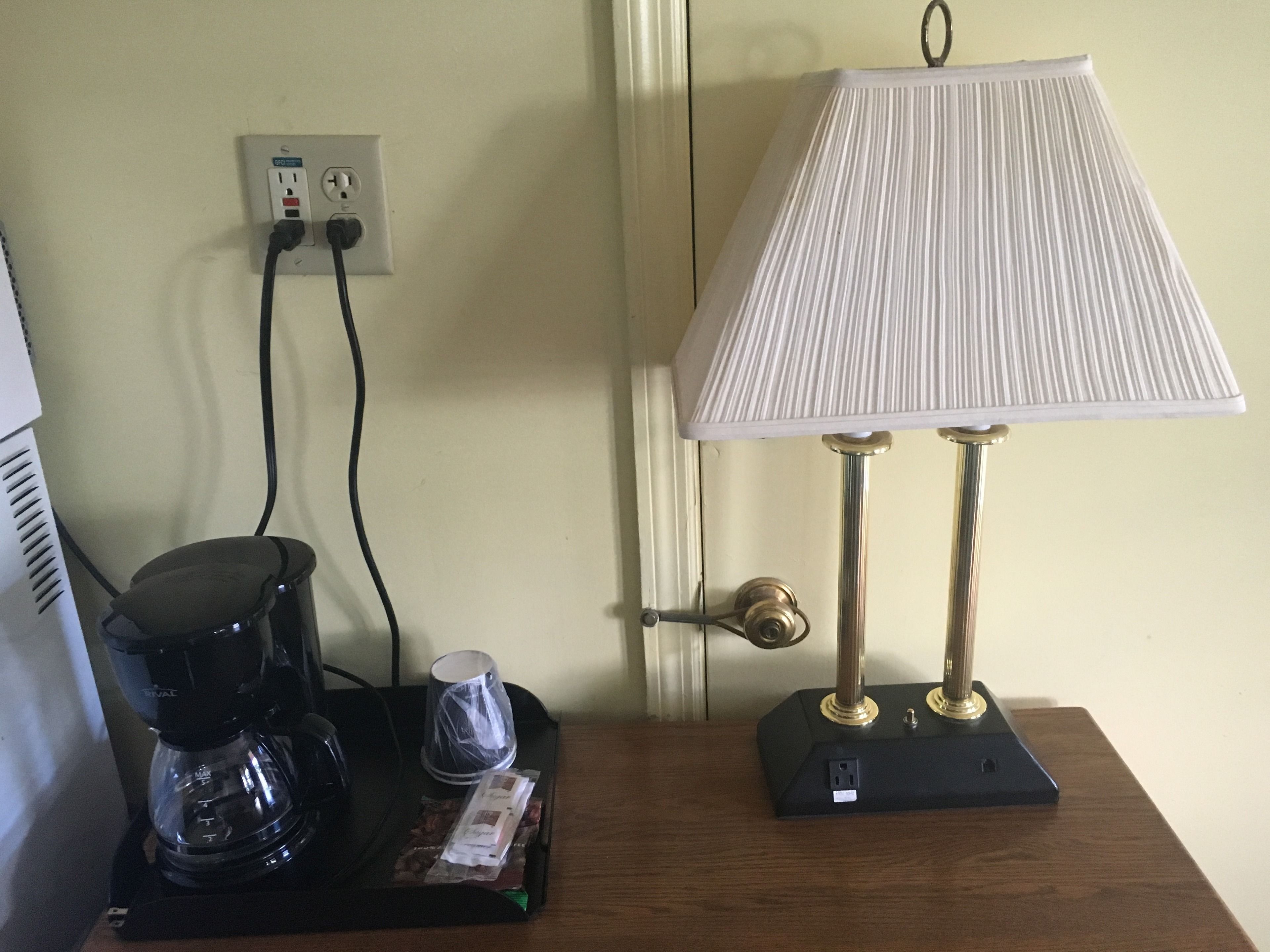 Una cafetera, una lámpara y un enchufe sobre una mesa de madera.