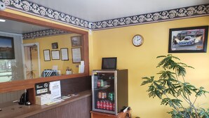 A reception area with a wooden counter, a clock, a refrigerator stocked with beverages, and a potted plant. - Norwalk Inn (Norwalk)