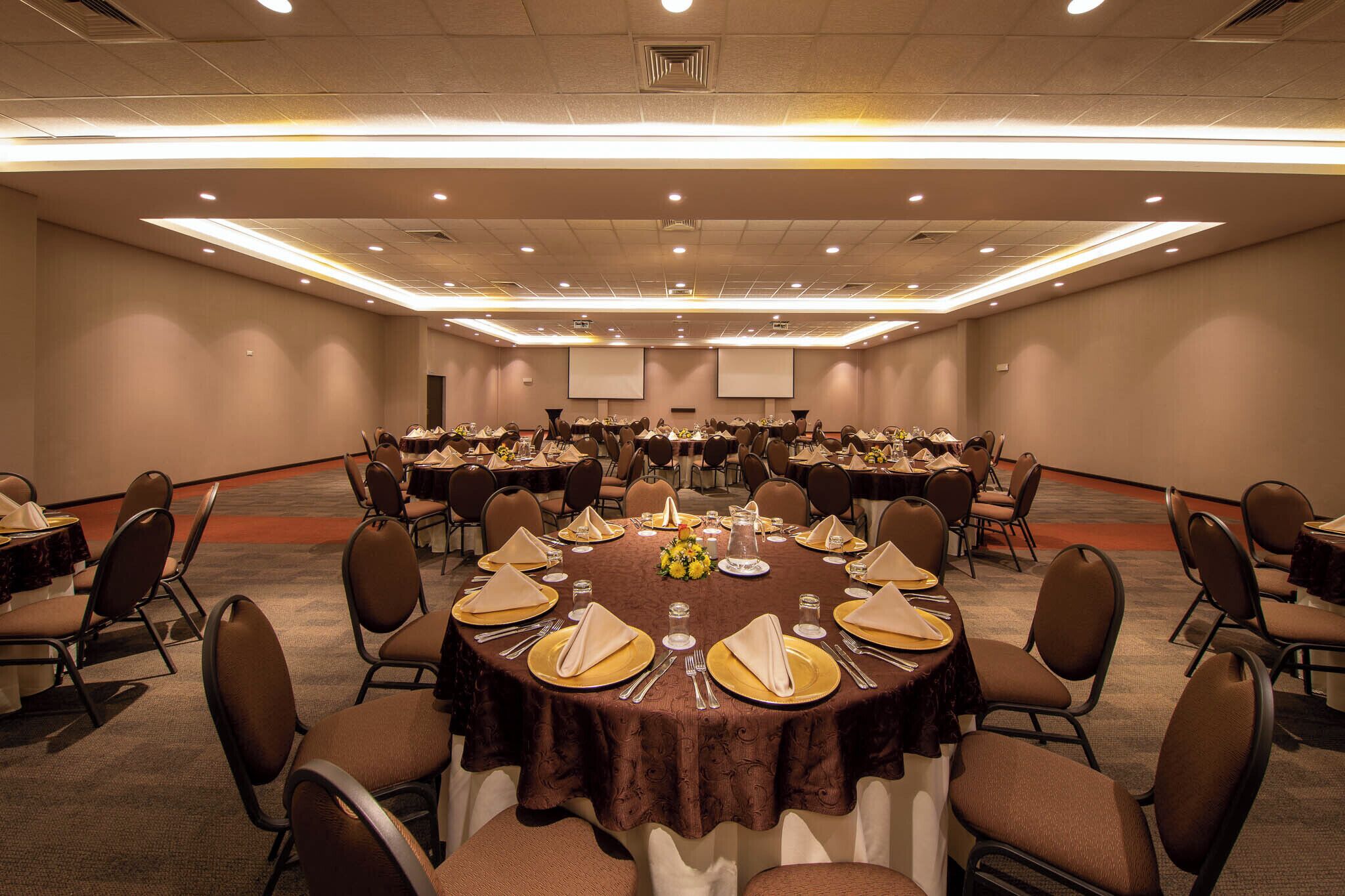 A conference room with round tables set for a meeting, equipped with chairs and tables, and a projector screen at the front.