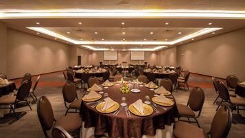 A conference room with round tables set for a meeting, equipped with chairs and tables, and a projector screen at the front.