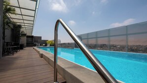 An outdoor swimming pool with a wooden deck and metal railing, overlooking a cityscape. - Casa Andina Select Tacna (Tacna)