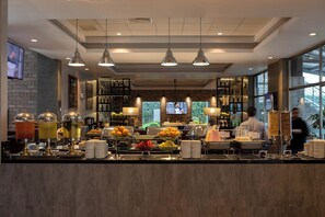 A buffet area with various food and drink options, including fruit, beverages, and a coffee station.