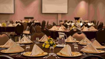 Une salle de banquet où les tables sont dressées pour un événement formel, avec une décoration soignée, des verres et une carafe d’eau.
