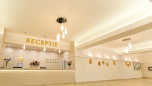 Zona de recepción de un hotel con mostrador, certificados enmarcados en la pared y un techo con luces colgantes.