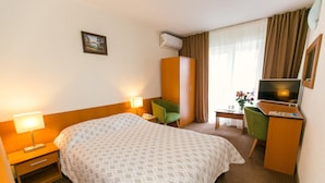 Habitación de hotel con cama, escritorio, silla, televisión y aire acondicionado.