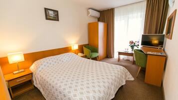 A hotel room with a bed, a desk, a chair, a television, and an air conditioning unit.