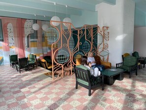 A modern lounge area with a patterned floor, green and black upholstered chairs, and a decorative metal partition with spherical designs. - Mures Saturn (Saturn)