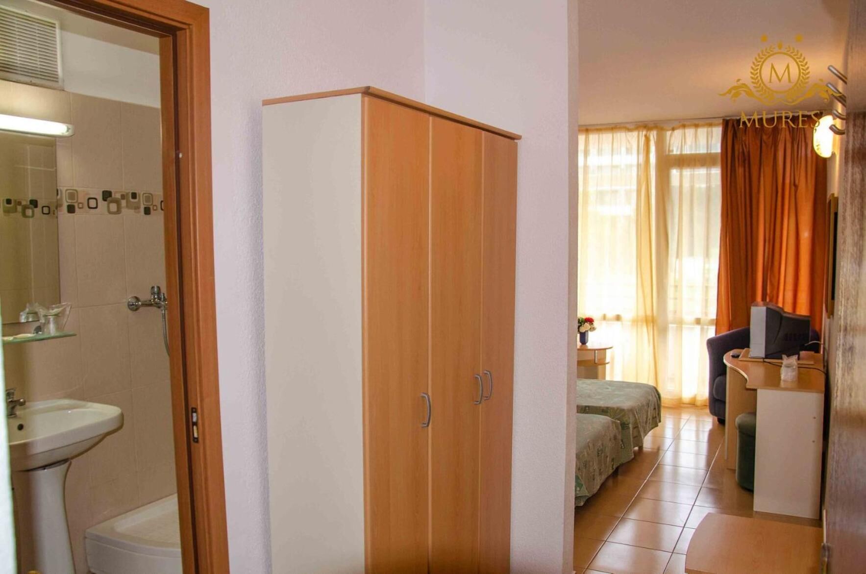 A hotel room with a bathroom, a wardrobe, a desk with a computer, and a bed.