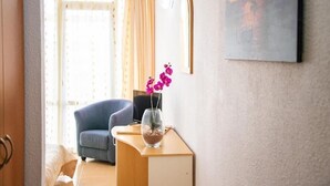 A hotel room with a wooden desk, a blue chair, a vase with flowers, a television, and a painting on the wall. - Mures Saturn (Saturn)