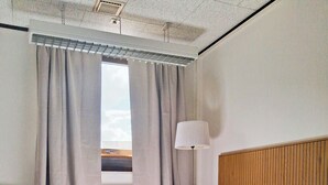 A hotel room with a bed, a window with curtains, a lamp, and a ceiling fan.