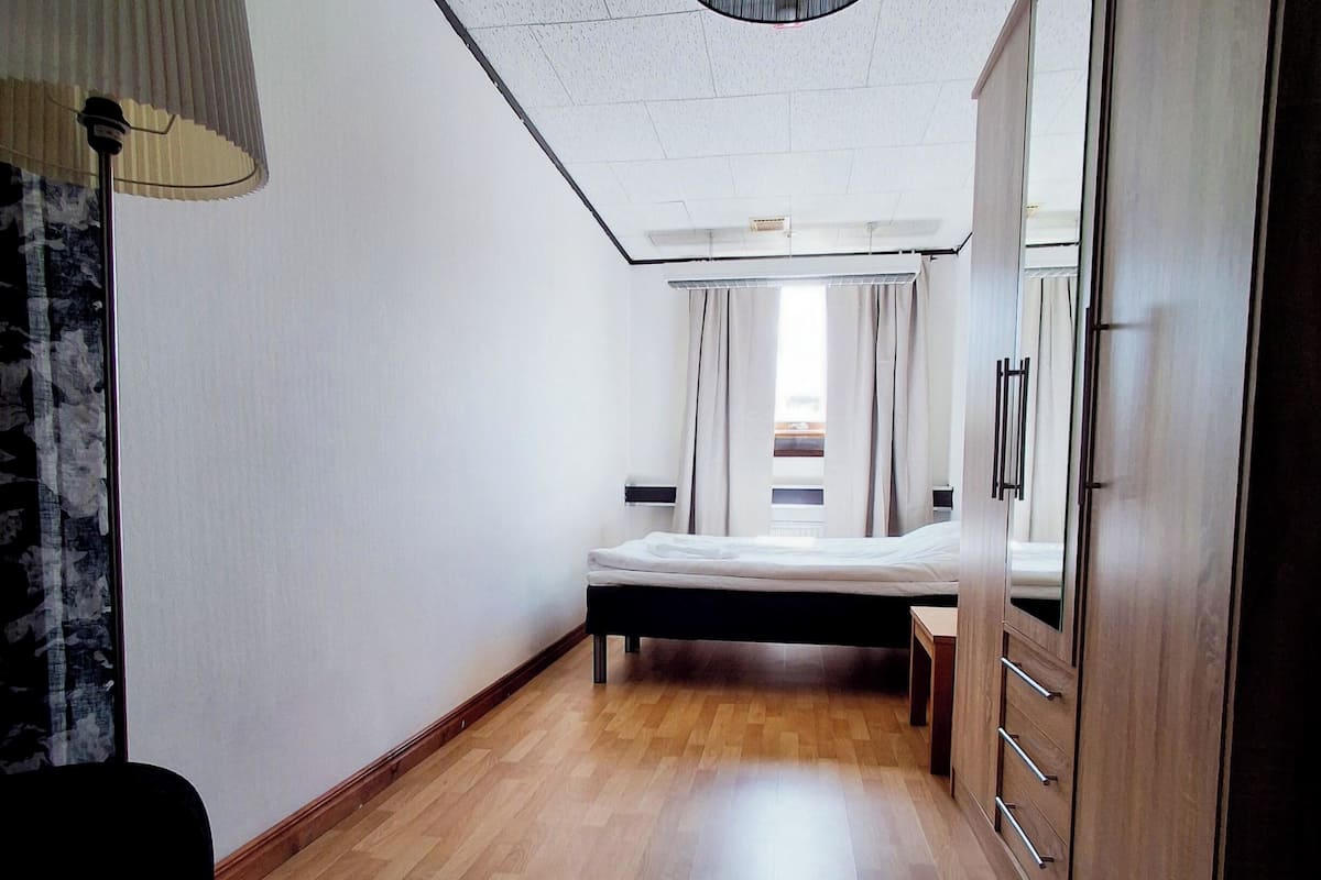 A bedroom with a wooden floor, a bed, a wardrobe, and a ceiling fan.