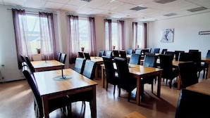 A conference room with multiple tables and chairs, large windows with curtains, and a ceiling with ventilation.